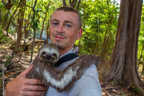 Young man with sloth in arms in rainforest Amazonas Brazil. photo