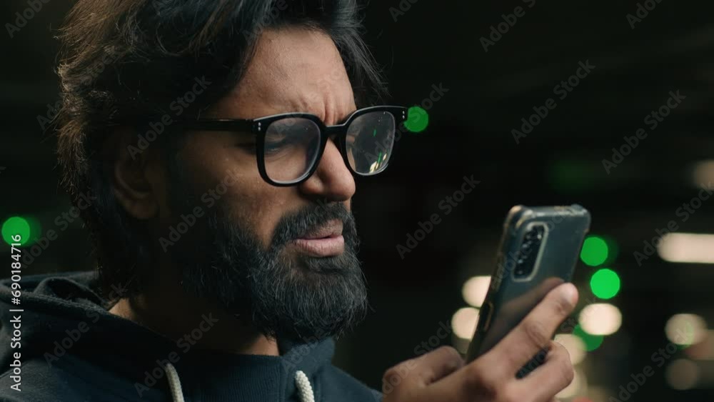 Stressed shocked disappointed sad Arabian man in glasses read bad news in smartphone millennial Indian bearded male hold mobile phone stress by SMS rejection message failure lost crash at parking lot