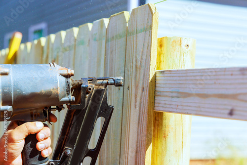 By using an air nail gun, he constructs sections of wooden fence around his yard photo