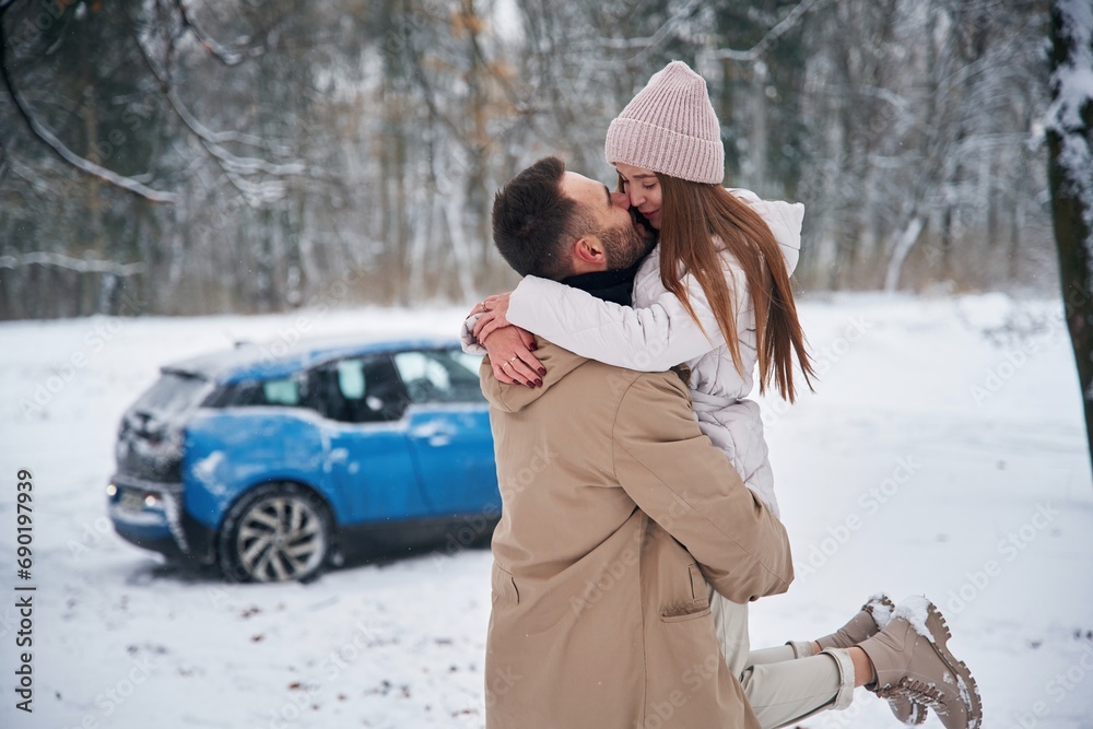 Smiling, having fun. Happy couple having a walk in winter forest. Blue car is parked