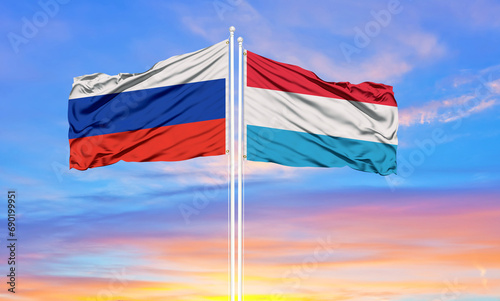 Russia and Luxembourg two flags on flagpoles and blue sky.