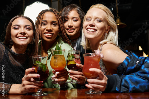 young and glamorous women with delicious cocktails smiling at camera, entertainment in bar