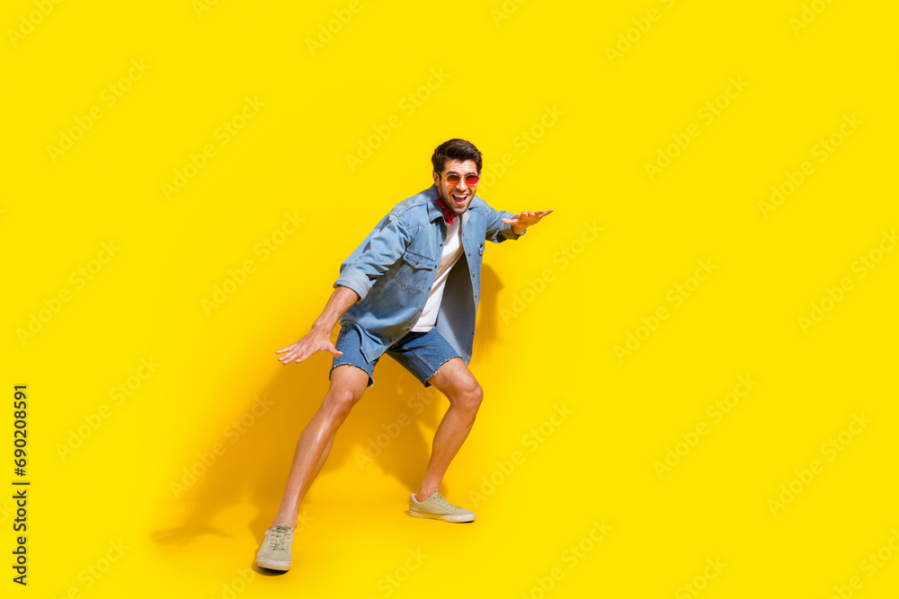 Full body photo of funky handsome man dressed denim shirt shorts surfing on imaginary board isolated on vivid yellow color background