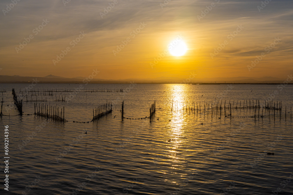 A lake with fish nets and sunny path against the backdrop of an orange sunset