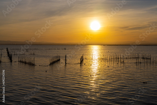 A lake with fish nets and sunny path against the backdrop of an orange sunset © Tatiana Kuklina