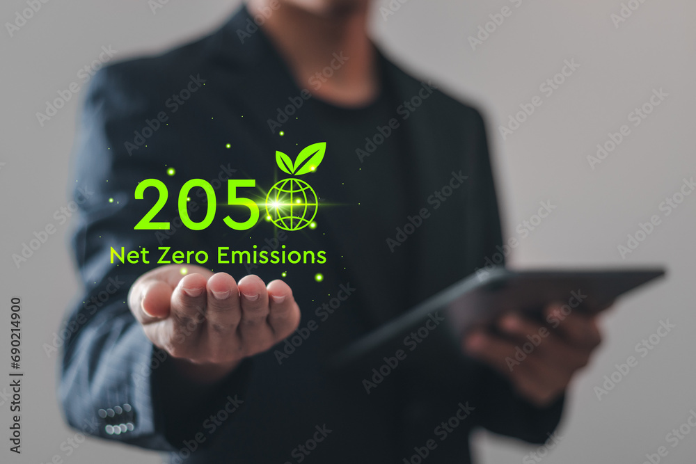 Net zero emissions by 2050. Businessman holding virtual Net Zero icon to change climate and net zero greenhouse gas emissions target. Sustainable development and green business concept. - obrazy, fototapety, plakaty 