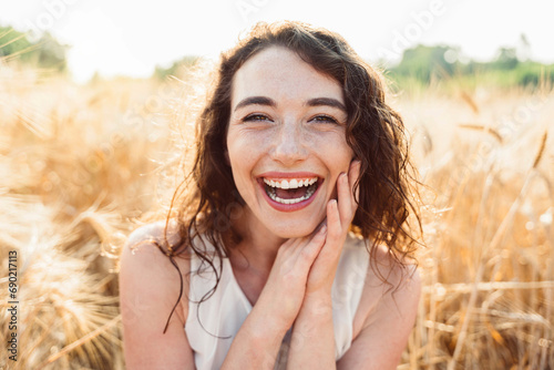Happy beautiful woman smiling at camera in a wheat field - Delightful female enjoying summertime sunny day outside - Wellbeing concept with confident girl laughing in the nature photo