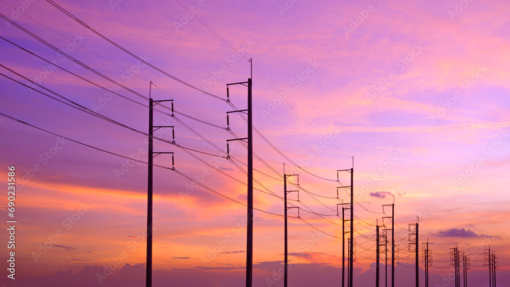 Silhouette row of electric poles with cable lines against colorful sunset sky background, low angle and widescreen view