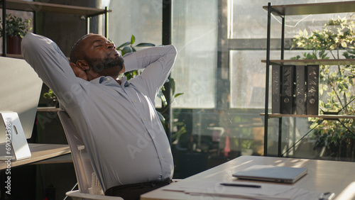 Relaxed African American mature businessman senior happy man finish computer work close laptop relaxing in sunny warm comfortable office male specialist stretch muscles put hands behind head day end