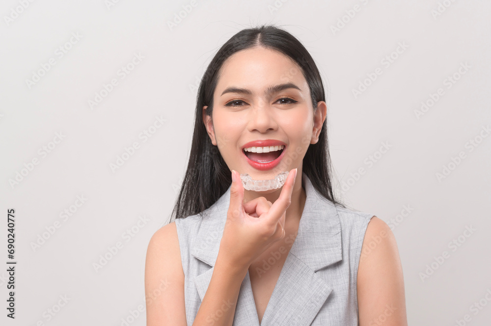 Young smiling woman holding invisalign braces in studio, dental healthcare and Orthodontic concept. - obrazy, fototapety, plakaty 
