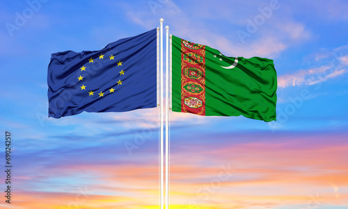 European Union and Turkmenistan  two flags on flagpoles and blue cloudy sky . Diplomacy concept, international relations