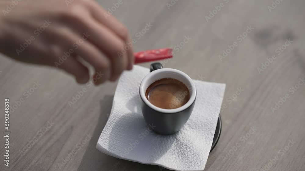Hand pouring sugar in black cup of coffee on cafe bar table, selective focus cinematic slow motion shot Hand pouring sugar in black cup of coffee on cafe bar table, selective focus cinematic slow motion shot