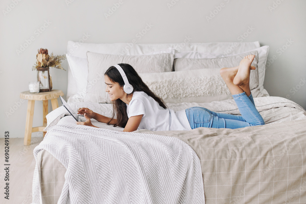 Adorable pre-teen girl in wireless headphones lying on bed with digital tablet device Adorable pre-teen girl in wireless headphones lying on bed with digital tablet device