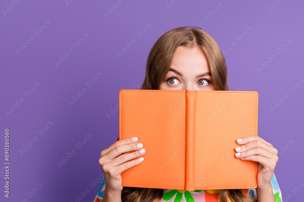 Portrait of funny shy girl dressed print t-shirt look out from book to empty space proposition isolated on violet color background Portrait of funny shy girl dressed print t-shirt look out from book to empty space proposition isolated on violet color background