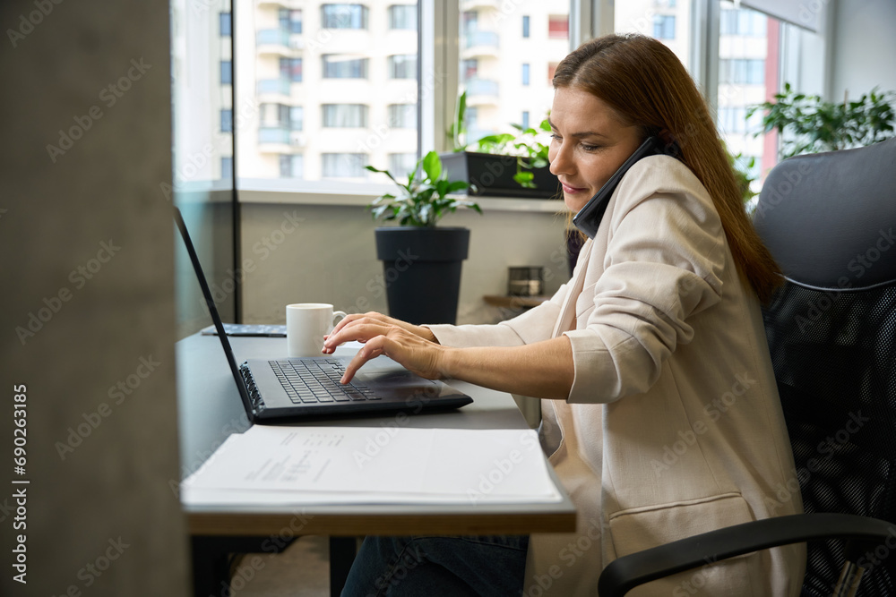 Beautiful woman sitting in office chair with mobile phone and laptop Beautiful woman sitting in office chair with mobile phone and laptop