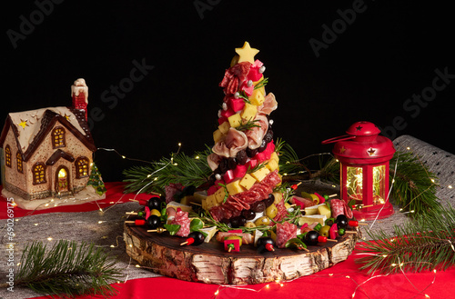 Appetizers board with different antipasti, charcuterie, snacks and cheese. Christmas tree of meat, sausage delicacies and cheese on a kraft wooden board. Christmas decor on black background
