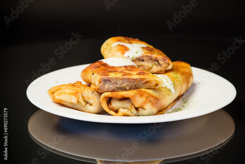 Thin fried pancakes with meat filling in a plate with sour cream and spices. © Peredniankina