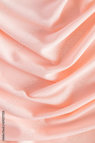 Soft pleats of peach colored satin textiles. Luxury abstract textile background design. Vertical view. Color of the Year 2024 peachy fuzz.
