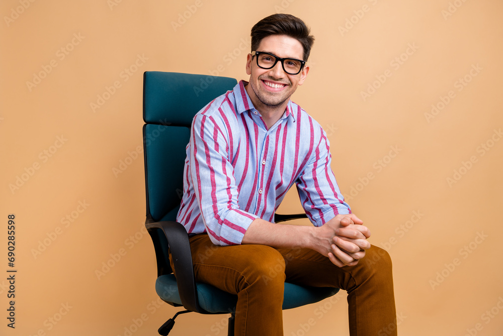 Photo of attractive cheerful man dressed trendy clothes sitting comfortable chair hiring recruitment isolated on beige color background Photo of attractive cheerful man dressed trendy clothes sitting comfortable chair hiring recruitment isolated on beige color background