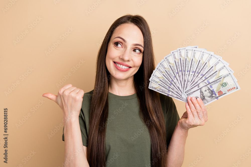 Portrait of smiling business lady wear khaki t shirt direct finger novelty holding banknotes shopaholic isolated on beige color background Portrait of smiling business lady wear khaki t shirt direct finger novelty holding banknotes shopaholic isolated on beige color background