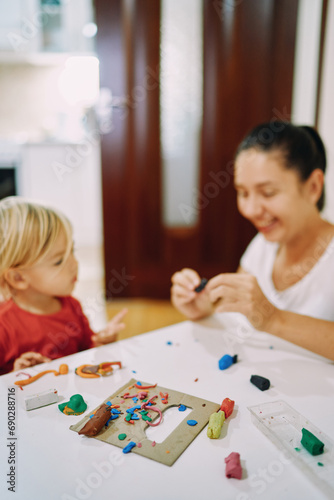Mom and her little daughter sculpt different figures from colored plasticine while sitting at the table