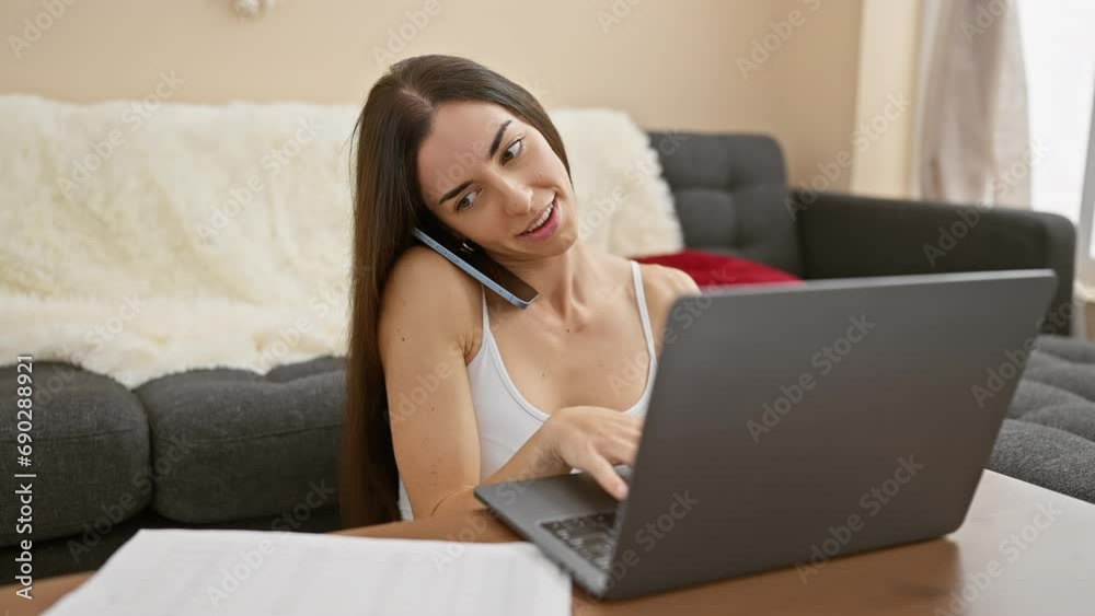 Joyous young hispanic woman, beautifully smiling, basks in comfort as she enjoys engaging talk via smartphone and laptop on the floor at home Joyous young hispanic woman, beautifully smiling, basks in comfort as she enjoys engaging talk via smartphone and laptop on the floor at home