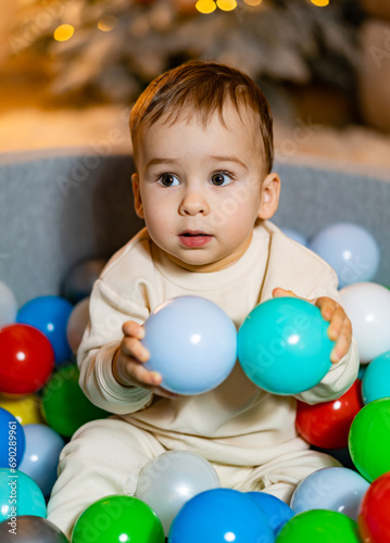 A baby sitting in a ball pit surrounded by balloons. Baby Having Fun in a Colorful Ball Pit