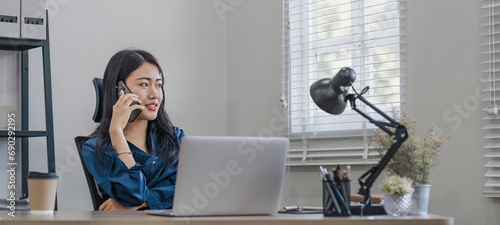 Young happy asian woman talking on mobile phone, relaxing while working at co-workspace.
