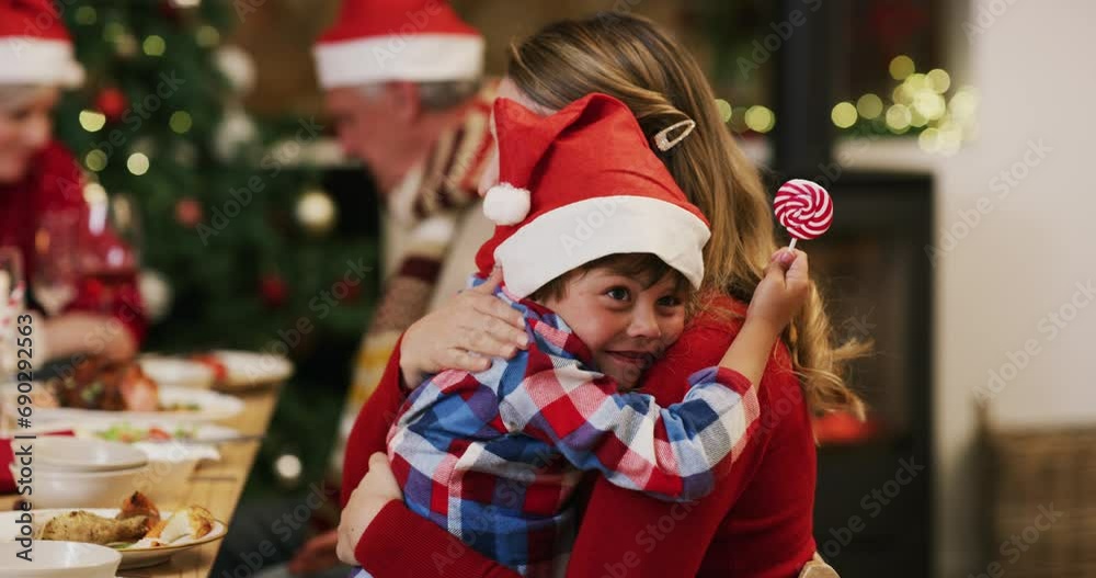 Happy boy, mother and hug on Christmas for love, care or bonding together in embrace at home. Little child or kid hugging mom with hat and candy lollipop at dining table for holiday weekend at house