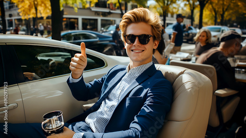 stylish young man in sunglasses gives a thumbs up while sitting in a luxury car, looking confident and happy, with a city street behind him © weerasak
