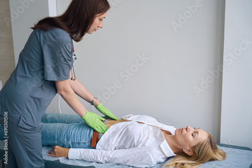 Family doctor performing abdominal exam of mature woman photo