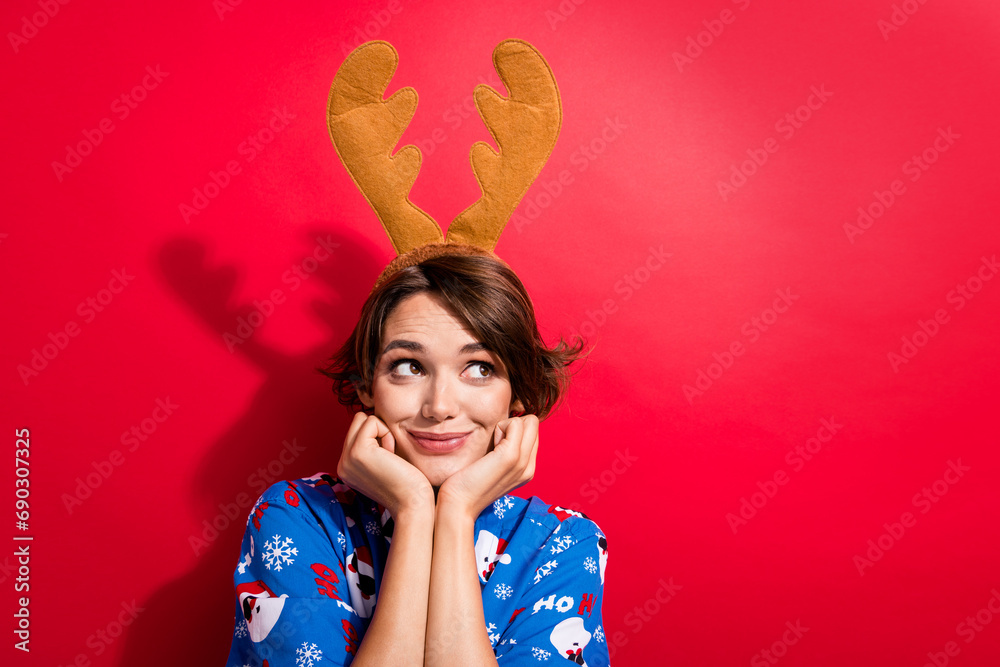 Photo of minded lovely lady arms touch cheeks look empty space imagine deer horns headband isolated on red color background