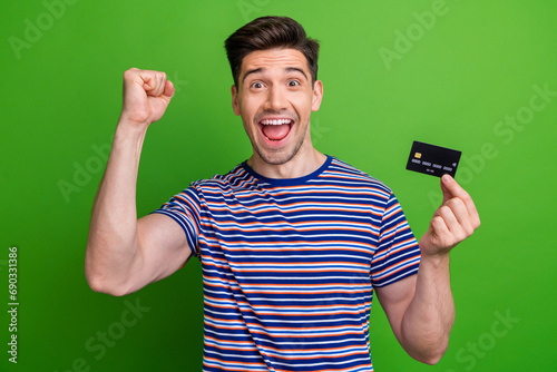 Photo of overjoyed cheerful person raise fist arm hold demonstrate debit card isolated on green color background