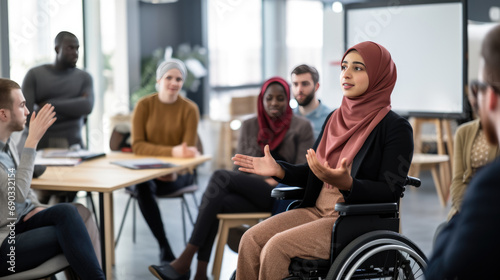 Meeting in an accessible office environment where a woman in a wheelchair and wearing a hijab is actively participating and engaging with her colleagues.