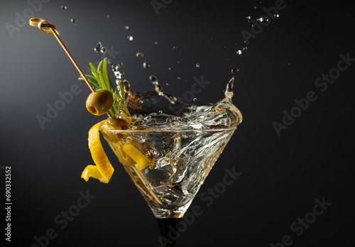 Classic dry martini cocktail with green olives, lemon peel, and rosemary on a black background.