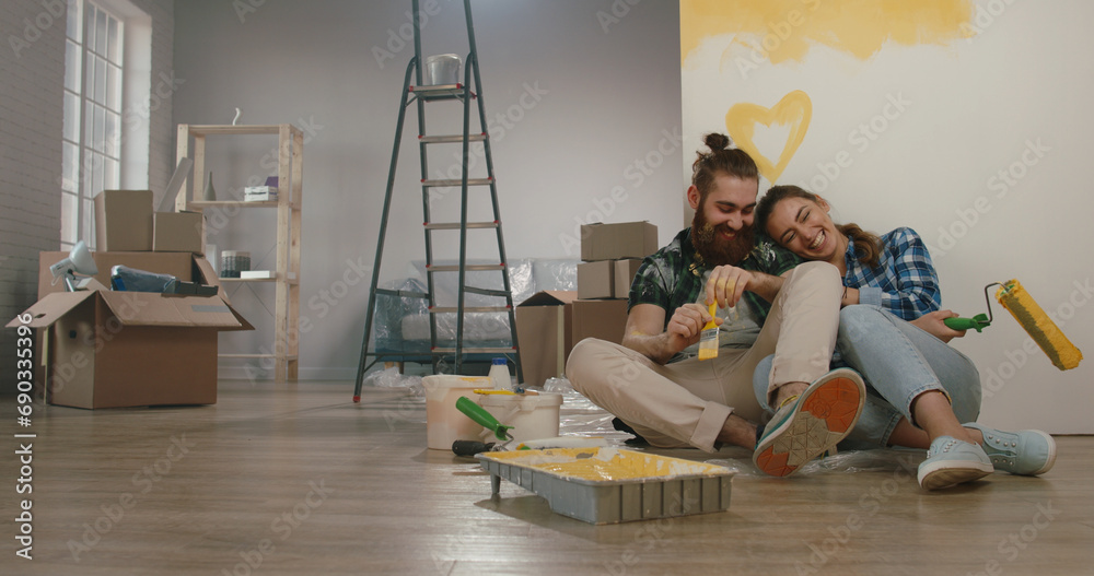 Fototapeta premium Newlywed caucasian couple is renovating their new home, painting the walls and positively smiling - new life, young family, mortgage concept 