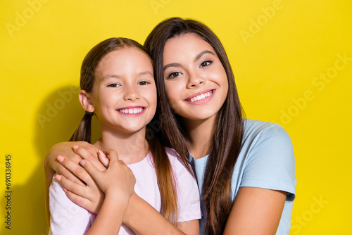 Photo of charming sweet little sisters wear t-shirts cuddling smiling empty space isolated yellow color background photo