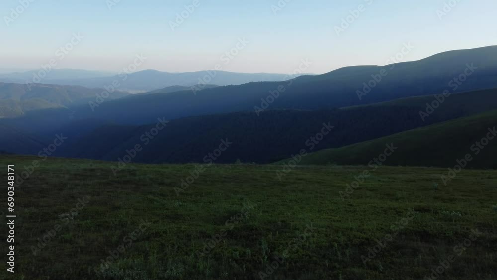 View from a drone of the mountains stretching into the blue into the distance. Green alpine vegetation is visible in the foreground. View from a drone of the mountains stretching into the blue into the distance. Green alpine vegetation is visible in the foreground.