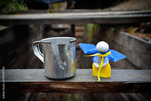 War in Ukraine. Belongings of a Ukrainian warrior defending his country during the war such as iron mug deformed by fragments of enemy shells and Ukrainian traditional angel doll as amulet from death.