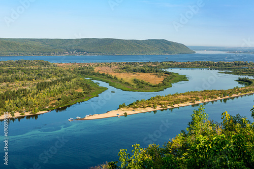 Zhiguli Mountains, Volga River and quiet backwater near the city of Samara, Russia. Blue water, sandy shore, tree, bush, motor boat, yacht. Quiet summer morning with light sky.