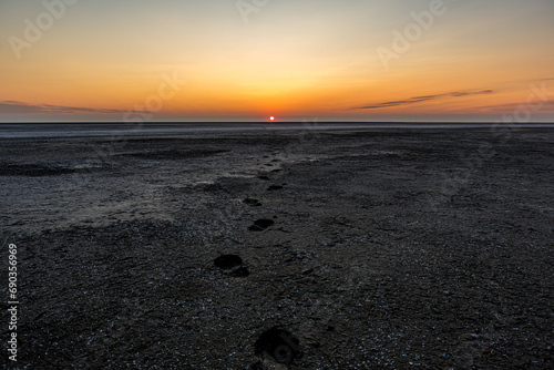 Sunrise or sunset on the salt lake Bulukhta (Russia). Human footprints going towards the sun at golden hour with the sun in the background. Evening or morning.