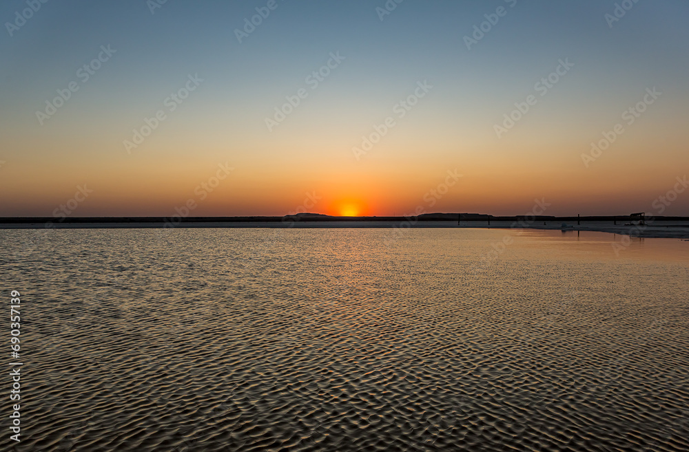 Fototapeta premium Sunset or sunrise on salt lake Baskunchak (Russia). Bright sun in a cloudless sky, calm brine in the saline. Morning or evening in summer, autumn or spring.