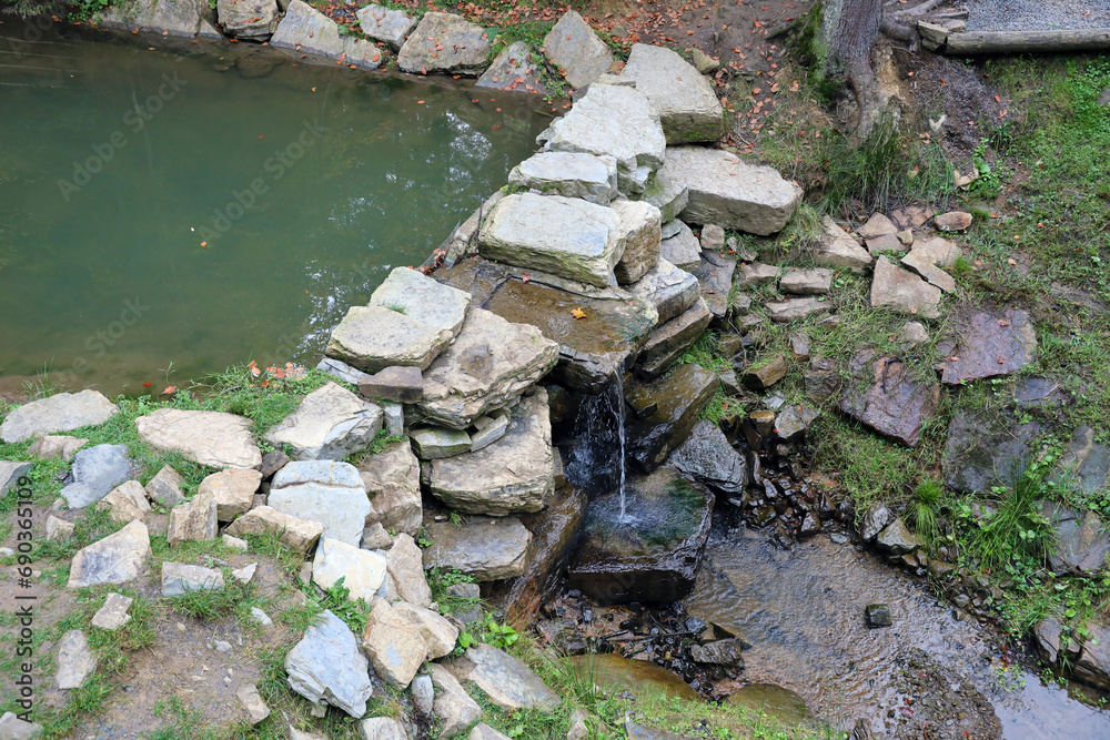 Close up of a small waterfall spilling over moss covered rocks in regional park. Handmade river waterfall of small stones Close up of a small waterfall spilling over moss covered rocks in regional park. Handmade river waterfall of small stones