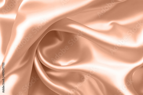 Abstract background, folds of silk fabric in peach fuzz color.