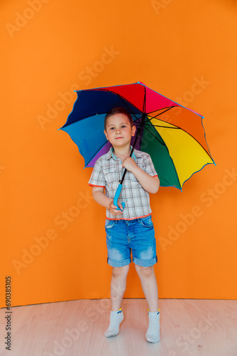 Boy standing under colorful rain umbrella on orange background