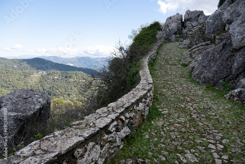 Stone pathway in a mountainous landscape with greenery and clear skies. © Joseph Creamer