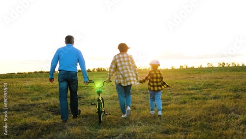 Mum and dad with youngster enjoy stroll with bike in nature. Inquisitive kid explores hidden trails of countryside with parents on sunny day. Active family weekend in rural area during summer season