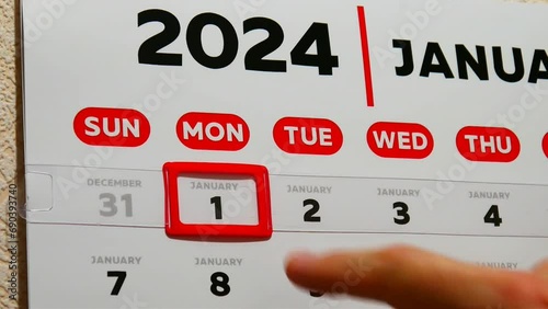 Close-up of a male finger moving a red cursor to the 1st January of the wall calendar 2024 photo