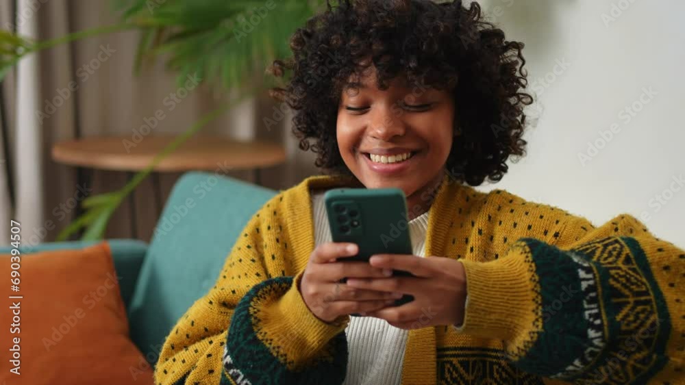 African girl holding smartphone touch screen typing scroll page at home. Woman with cell phone surfing internet using social media apps playing game. Shopping online Internet news cellphone addiction