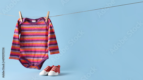 Baby booties and bodysuit hanging on rope against light blue background with space for text